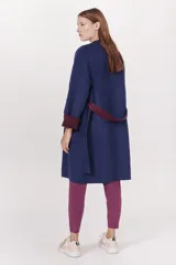 Tapado de paño azul marino con cuello solapa y mangas amplias. Presenta un cinturón de tela color bordó anudado a la cintura y puños doblados que dejan ver el forro bordó.