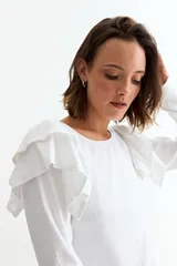 Remera de manga larga en color crudo, confeccionada en tejido acanalado, con detalle de volados en los hombros y cuello redondo.