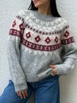 Sweater de punto con diseño nórdico en el canesú, de cuello redondo y manga larga. Presenta una combinación de colores gris, crudo y bordó con textura suave.