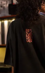 Remera de manga corta con cuello redondo y calce oversize, color negro con efecto lavado. Presenta un estampado frontal gráfico con motivos musicales y tipografía en tonos rojos y blancos.