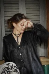 Camisa de seda negra con acabado satinado, corte amplio y estilo boho chic. Presenta cuello en V con cierre frontal de botones, mangas largas abullonadas con puños abotonados y detalles de frunces en hombros y espalda.
