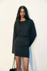 Vestido corto de manga larga confeccionado en punto elástico de color negro, con escote redondo, cuerpo holgado y falda entallada.