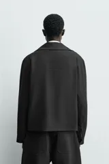 Sobrecamisa relaxed fit de Zara confeccionada en tejido negro con estructura diagonal. Presenta cuello subido, manga larga, bolsillos de vivo en la cadera y cierre frontal con cremallera.