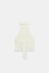 Top de cuello halter color blanco, con múltiples volantes en cascada en todo el frente y la espalda descubierta con cierre de botones y lazada en el cuello.