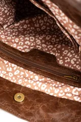 Bolso tipo tote bag color marrón, confeccionado en gamuza vegana con detalles de tiras y asas de hombro en cuero sintético brillante. Incluye una placa metálica pequeña con el logo de la marca en el frente.