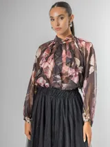 Camisa de seda italiana con estampado floral en tonos rosados, marrones y verdes. Presenta cuello alto con volados que caen en cascada sobre el frente y mangas largas abullonadas con puños ajustados.