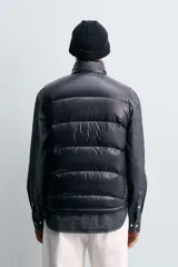 Chaleco acolchado de corte regular, confeccionado en tejido técnico repelente al agua. Presenta cuello subido, cierre frontal de cremallera y bolsillos laterales con cierre oculto. Relleno de plumón y pluma.