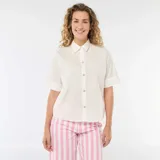 Camisa de corte holgado en color blanco, con cuello clásico, mangas cortas con dobladillo y cierre frontal con botones dorados en forma de estrella.