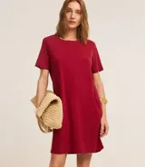 Vestido corto marrón oscuro, estilo camiseta, con escote redondo, mangas cortas y bolsillos laterales. El bajo es redondeado.