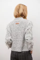 Buzo de punto color beige con cuello redondo, mangas largas con flecos decorativos y diseño de trenzas en el frente.