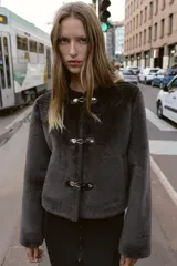 Chaqueta de cuello redondo y manga larga con tejido exterior efecto pelo e interior efecto ante. Presenta bolsillos delanteros de vivo y cierre frontal con alamares metálicos.