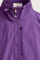 Chaqueta canguro técnica de corte relaxed fit en color violeta, con cuello subido ajustable, cierre frontal de cremallera parcial, manga larga y bolsillos frontales con cierre y tipo canguro.