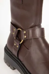 Bota estilo biker de cuero sintético color negro, con suela tipo plataforma dentada. Presenta una tira decorativa con argolla metálica y apliques de tachas en el tobillo.