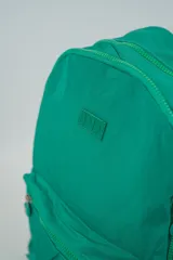 Mochila de color azul con un bolsillo frontal con cierre de cremallera y dos bolsillos laterales abiertos. Tiene correas ajustables para los hombros y un asa superior.