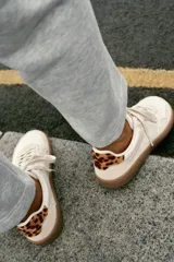Zapatillas deportivas barefoot de color blanco con detalles en beige y suela de goma marrón. Presentan cordones blancos y detalle de estampado animal print de leopardo en la talonera.