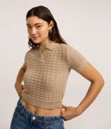 Blusa tipo polo de punto texturizado color beige, con cuello camisero, cierre frontal de botones, manga corta ajustada y diseño corto al cuerpo.