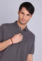 Remera tipo polo de manga corta en color gris oscuro, con cuello clásico y cierre frontal de dos botones. Presenta un pequeño logo bordado en el pecho.