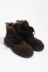 Botín de caña baja confeccionado en gamuza color marrón oscuro, con interior forrado en pelo sintético. Presenta cierre mediante cordones frontales, puntera redonda y suela de goma dentada en color negro.