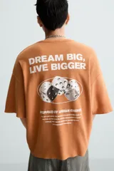 Camiseta boxy fit de punto tejido en hilatura de algodón, color terracota, con cuello redondo y manga corta. Estampado frontal de dados en tonos grises y blancos dentro de un óvalo.