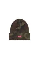 Gorro tipo beanie de tejido acanalado con diseño de camuflaje en tonos verdes y marrones. Presenta una etiqueta rectangular roja con el logo de la marca en la parte frontal.