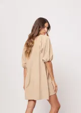 Vestido corto color beige, de corte oversize, con escote en V y mangas globo. Incluye cinturón marrón con hebilla dorada.