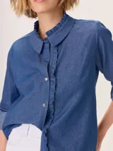 Camisa de algodón con cuello clásico y detalle de volados en la cartera delantera. Presenta mangas largas con puños abotonados y un diseño de corte recto.