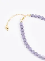 Collar de cuentas de vidrio color ámbar con un charm dorado en forma de llama en el centro. Incluye cadena de extensión y cierre de mosquetón.