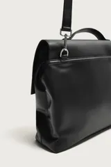 Bolso de mano y hombro color negro, con diseño estructurado, solapa frontal y cierre metálico. Cuenta con asa superior de mano y un compartimento principal amplio.