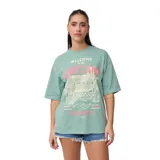 Remera verde con estampado de cabaña de playa, palmeras y tablas de surf.