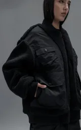Campera estilo bomber unisex, confeccionada en una combinación de corderito sintético y paneles de ripstop. Presenta un diseño utilitario con múltiples bolsillos frontales con cierres y broches a presión, cuello, puños y ruedo en ribb elástico.