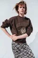 Buzo de corte oversized con cuello redondo, confeccionado en tejido con interior suave. Presenta hombros caídos, puños y bajo acanalados, y un diseño gráfico estampado en el pecho con estilo universitario.