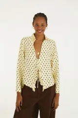 Blusa de lunares color amarillo con diseño de puntos y detalles oscuros, cuello camisero y cierre frontal con cordones para atar.