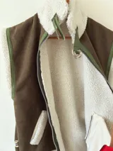 Chaleco negro de cuerina con interior de corderito sintético, bolsillos frontales y hebillas decorativas.