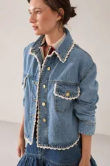 Campera de jean con corte regular estilo camisera, con detalles tejidos a mano en crochet a contratono en los bordes, cuello y bolsillos frontales. Cuenta con cierre frontal de botones metálicos dorados.