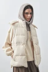 Chaleco puffer negro con diseño acolchado, capucha desmontable y cierre frontal. Cuenta con cordones ajustables en la cintura y bolsillos laterales.