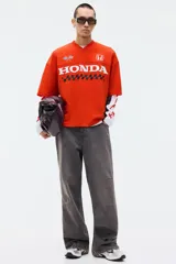 Remera de malla color rojo, con cuello en V, mangas cortas y corte oversized. Cuenta con diseño estampado frontal de Honda con banderas a cuadros y el logo de la marca.