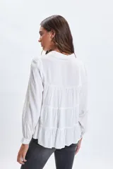 Camisa blanca de corte holgado con diseño de paneles escalonados, cuello clásico, cierre frontal con botones y mangas largas con puños.