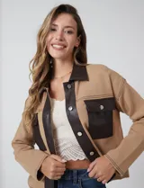 Chaqueta de corte recto y silueta boxy, confeccionada en tejido de punto color beige con detalles en cuero sintético marrón en solapas, cartera frontal y bolsillos. Presenta cierre central con botones metálicos plateados, bolsillos frontales con solapa y costuras decorativas horizontales.
