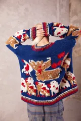 Sweater de lana tejido y bordado a mano, de calce holgado con cuello redondo y puños. Presenta un diseño artesanal con motivos figurativos en colores azul, beige, blanco y rojo.