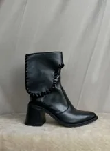 Botas cortas de gamuza color marrón, con taco cuadrado y punta ligeramente elevada. Presentan un detalle de costura trenzada en el borde superior de la caña.