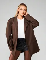 Blazer oversized color marrón chocolate con diseño de rayas finas verticales (pinstripe). Presenta solapas clásicas, cierre frontal con botones y bolsillos delanteros con solapa.