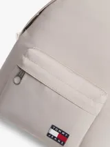 Mochila Tommy Jeans de color beige, diseño compacto y curvo, con compartimento principal con cierre de cremallera, bolsillo frontal con cremallera y parche con el logo de la marca. Cuenta con asas ajustables y acolchadas.