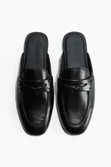 Mules estilo mocasín de cuero negro, con punta de almendra y detalle de tira penny con perforaciones decorativas en el empeine. Diseño destalonado con forro de punto.