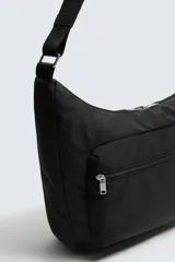 Bolso de hombro tipo hobo o media luna, confeccionado en tejido técnico negro. Presenta un bolsillo frontal con cierre y una correa ajustable para llevar al hombro.