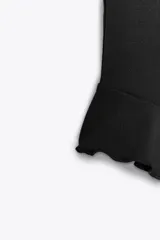 Top negro de cuello halter con lazada, escote recto y hombros descubiertos. Presenta un volante asimétrico en el lateral.