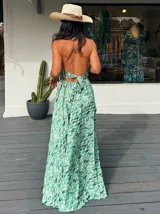 Vestido largo con estampado de hojas en tonos verde y blanco, con escote halter y espalda descubierta.