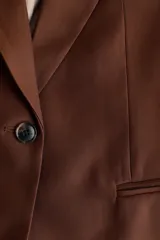 Blazer de manga corta de botonadura sencilla en color marrón, con solapas de muesca, cierre de un botón frontal, bolsillos delanteros ribeteados y forro interior.