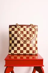 Bolso tipo tote de cuero trenzado a mano con diseño de damero en colores marrón y beige. Cuenta con doble asa trenzada y forro interior.