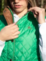 Chaleco capitoneado color rosa claro, con cuello alto, cierre frontal con botones a presión y logo bordado en el pecho.