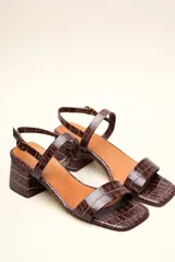 Sandalia de cuero vacuno color negro con textura de cocodrilo, taco cuadrado de 4 cm, punta cuadrada y dos tiras finas, una en el empeine y otra con hebilla en el tobillo.